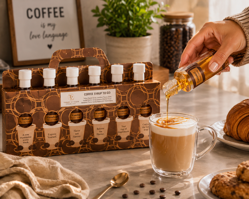 Tilz Collection Coffee Syrup Gift Set syrup being poured into a latte glass cup with gift box of six flavoured coffee syrups in background on kitchen counter with coffee beans croissant and cookies