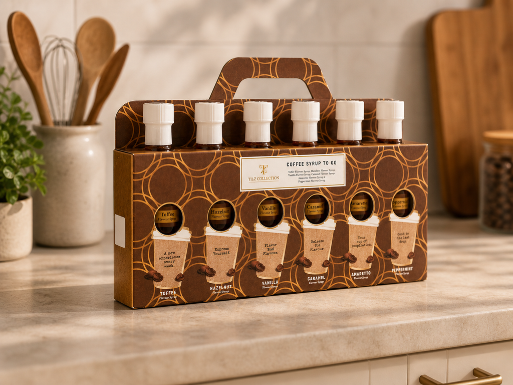Tilz Collection Coffee Syrup Gift Set side angle view of branded gift box with six coffee syrup bottles on kitchen counter with wooden utensils and plant in background