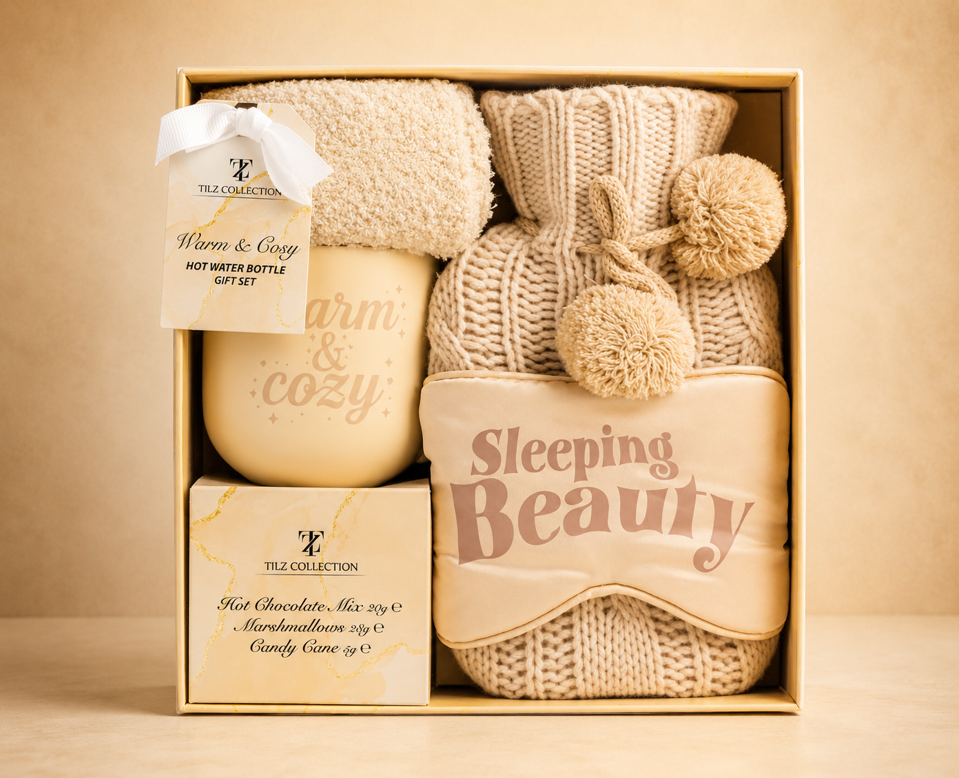 Tilz Collection Hot Water Bottle Gift Set for Her — front view of open kraft gift box with cream hot water bottle, Warm and Cosy mug, plush socks, Sleeping Beauty eye mask and hot chocolate treats neatly arranged